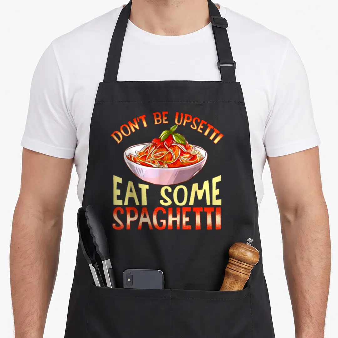 Upsetti pasta apron - Cartoon spaghetti bowl with red sauce and green basil under arched text EAT SOME SPAGHETTI — shown on a black cotton canvas apron against a white background