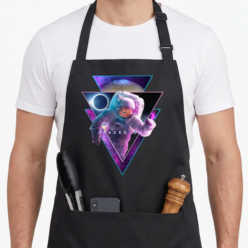 Astronaut cosmonaut apron - Astronaut in purple and blue triangles with black hole reflection and text spaced out — shown on a black cotton canvas apron against a white background