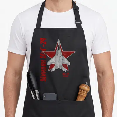 Mig airplane apron - MiG-29 jet top-down view on red star with vertical Cyrillic text and FULCRUM label — shown on a black cotton canvas apron against a white background