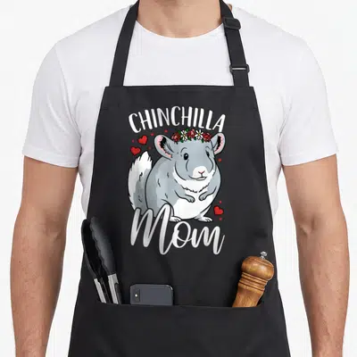 Retro chinchilla mom apron - Cartoon grey chinchilla with flower crown and red hearts framed by white text — shown on a black cotton canvas apron against a white background