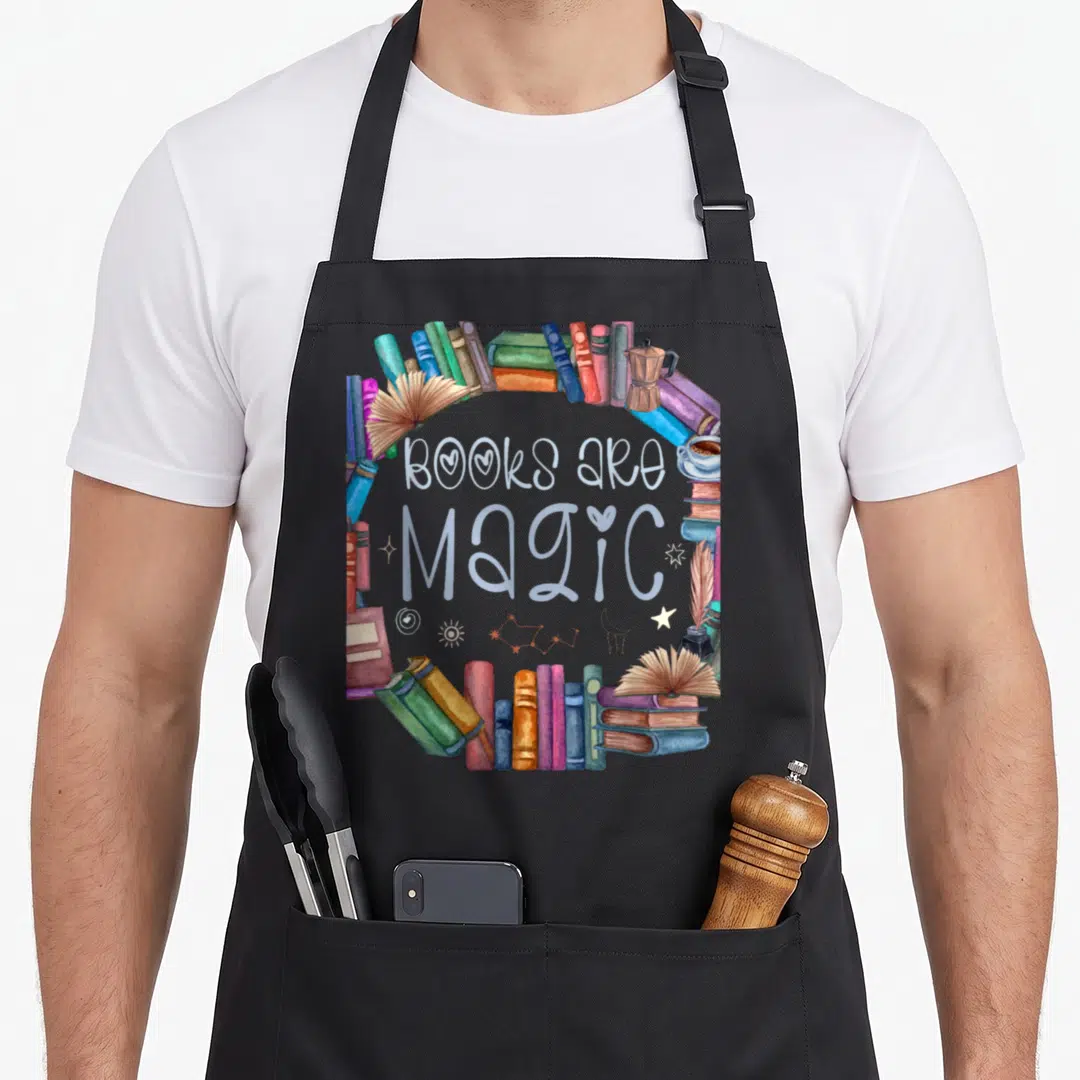 Bibliophile bookmark apron - Books Are Magic text surrounded by colorful watercolor books and coffee with celestial — shown on a black cotton canvas apron against a white background