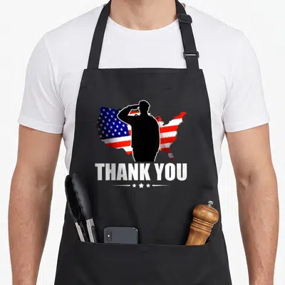 Service american flag apron - Black saluting soldier silhouette over red white blue US flag map with THANK YOU text — shown on a black cotton canvas apron against a white background