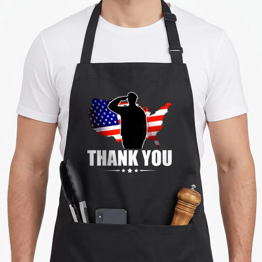 Service american flag apron - Black saluting soldier silhouette over red white blue US flag map with THANK YOU text — shown on a black cotton canvas apron against a white background