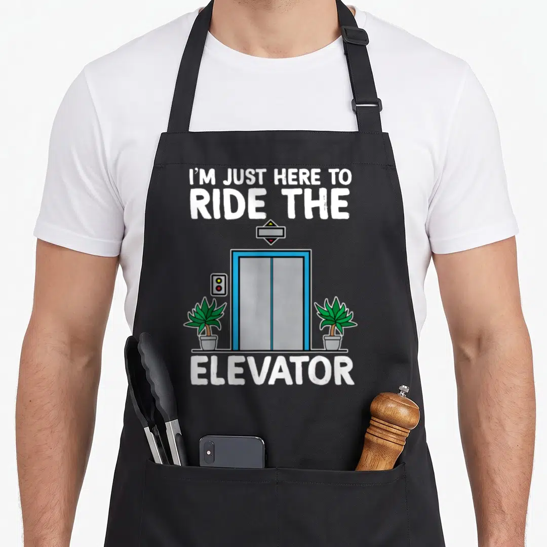 Elevator engineer apron - Cartoon blue elevator with two green potted plants and text I'M JUST HERE TO RIDE THE ELEVATOR — shown on a black cotton canvas apron against a white background