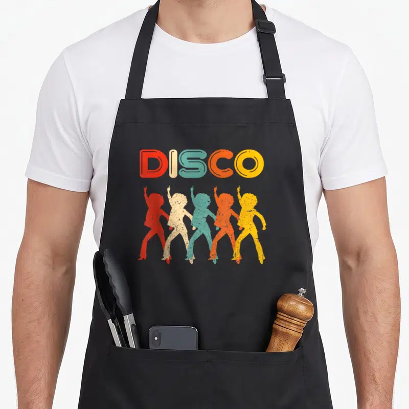 Disco 70s apron - Five colored disco dancer silhouettes under multicolored DISCO text in retro style — shown on a black cotton canvas apron against a white background