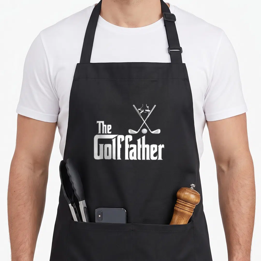 Golffather golf apron - White crossed golf clubs ball and The Golffather text in minimalist style — shown on a black cotton canvas apron against a white background