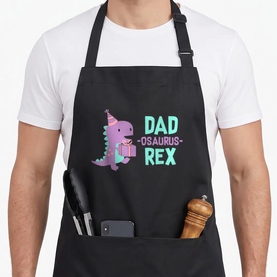 Birthday daughter family cooking aprons - Purple dinosaur with party hat holding gift next to stacked text DAD REX — shown on a black cotton canvas apron against a white background