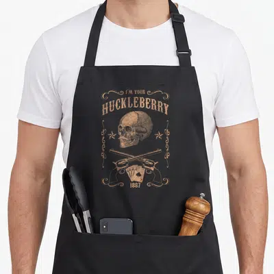 Huckleberry opera apron - Tan distressed skull crossed pistols playing cards 1887 text — shown on a black cotton canvas apron against a white background