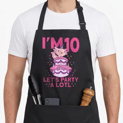 Bday axolotl 10th birthday apron - Pink axolotl in party hat on two-tier cake with I'M 10 text and confetti — shown on a black cotton canvas apron against a white background