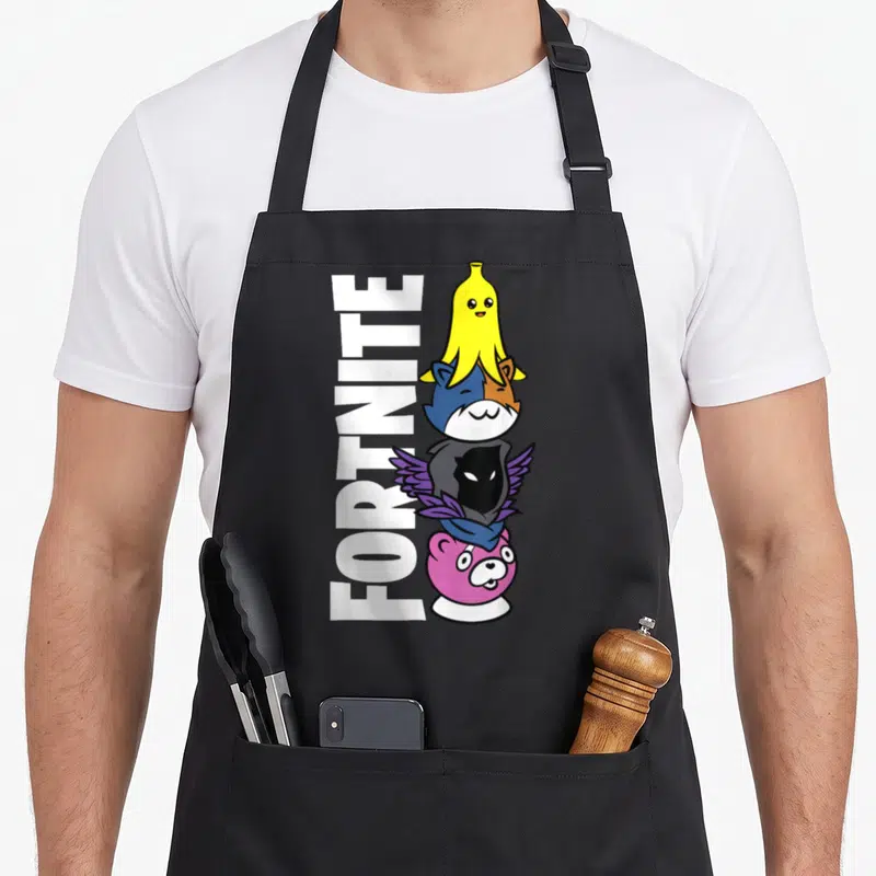 Cute crew apron - Vertical FORTNITE text next to a stack of four cartoon characters including a banana, fox, hooded — shown on a black cotton canvas apron against a white background