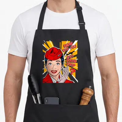 Trip flight attendant apron - Retro cartoon flight attendant in red hat with text HOW DID YOU GET THIS TRIP beside — shown on a black cotton canvas apron against a white background
