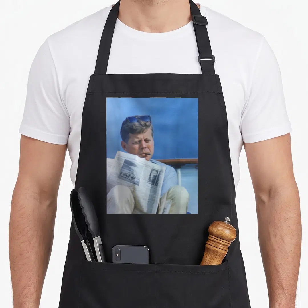 Jfk yacht apron - Photo of man with sunglasses and newspaper on blue background — shown on a black cotton canvas apron against a white background