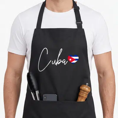 Cuba cuban pride apron - White script reading Cuba beside a heart shape filled with the Cuban flag colors — shown on a black cotton canvas apron against a white background