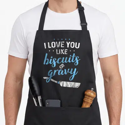 Gravy i love biscuits apron - Stacked white and blue text reading I LOVE YOU LIKE biscuits & gravy with five stars — shown on a black cotton canvas apron against a white background