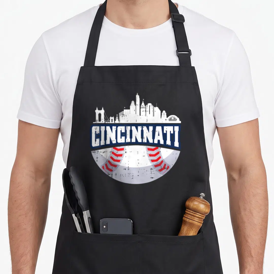 Cincinnati baseball apron - White skyline over navy banner reading CINCINNATI above a red-stitched baseball — shown on a black cotton canvas apron against a white background