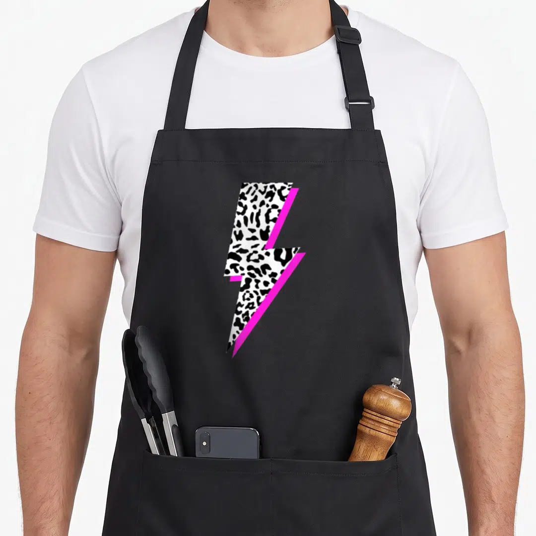 Lightning leopard print apron - Lightning bolt shape filled with black and white leopard spots and a magenta shadow — shown on a black cotton canvas apron against a white background