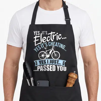 Cheating bicycle apron - White and blue text around electric bicycle silhouette with ribbon banner — shown on a black cotton canvas apron against a white background