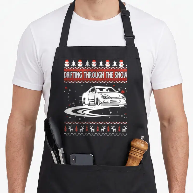 Car ugly christmas sweater apron - Pixel art white car drifting on snow tracks under red knitted text band framed — shown on a black cotton canvas apron against a white background