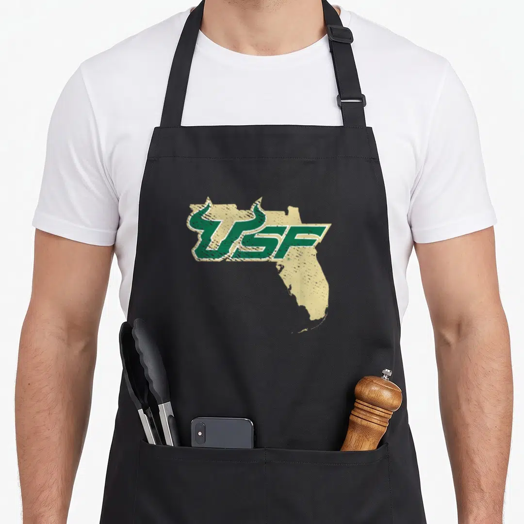 South florida apron - Distressed green USF text over tan Florida state silhouette shape — shown on a black cotton canvas apron against a white background