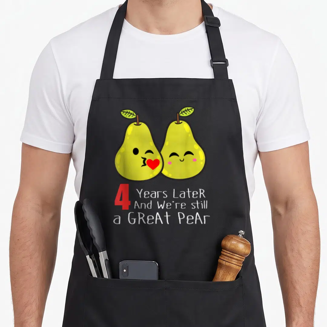 4th wedding aprons - Two cartoon yellow pears kissing a red heart above 4 Years Later Great Pear text — shown on a black cotton canvas apron against a white background