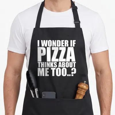 Cute wonder pizza apron - White stacked text reading I WONDER IF PIZZA THINKS ABOUT ME TOO..? — shown on a black cotton canvas apron against a white background