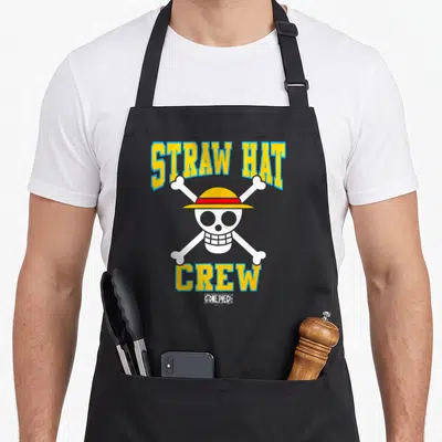 Hat anime apron - Skull with yellow hat and red band between STRAW HAT and CREW text — shown on a black cotton canvas apron against a white background
