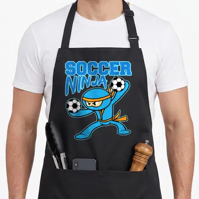 Soccer football apron - Blue cartoon ninja holding two soccer balls under stacked SOCCER NINJA text — shown on a black cotton canvas apron against a white background