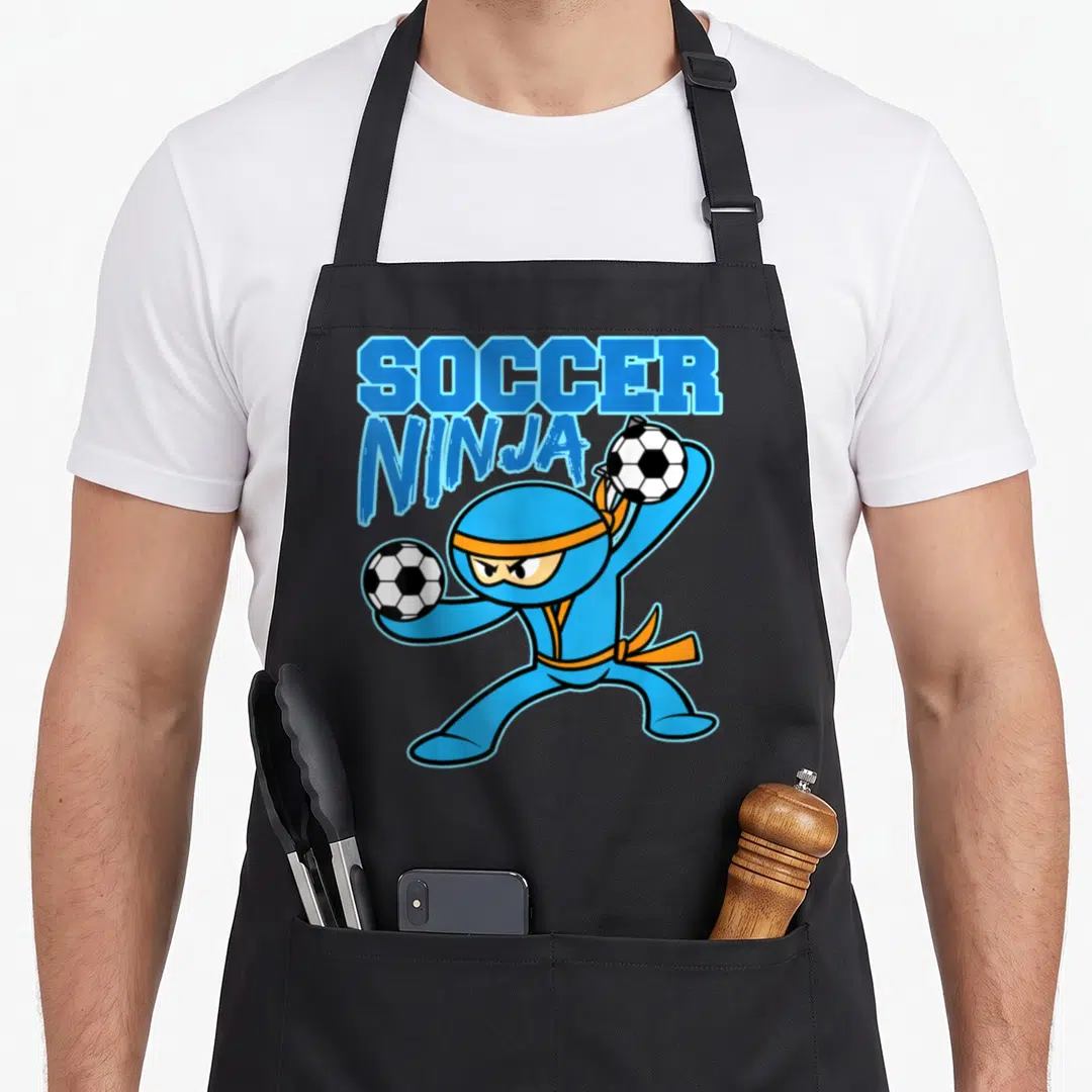 Soccer football apron - Blue cartoon ninja holding two soccer balls under stacked SOCCER NINJA text — shown on a black cotton canvas apron against a white background