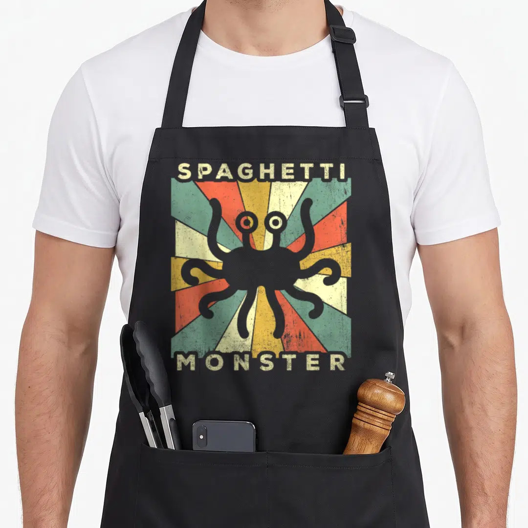 Monster spaghetti apron - Grey monster silhouette over red yellow green beige sunburst with SPAGHETTI MONSTER text — shown on a black cotton canvas apron against a white background