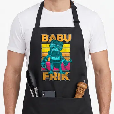 Rise frikadellen apron - Teal alien centered between orange BABU and FRIK text over yellow and pink stripes — shown on a black cotton canvas apron against a white background