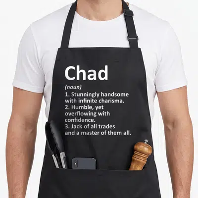 Chad definition birthday apron - White text defining Chad as stunningly handsome with infinite charisma and master — shown on a black cotton canvas apron against a white background