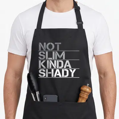 Slim but apron - Stacked white and grey text reading NOT SLIM KINDA SHADY on black background — shown on a black cotton canvas apron against a white background