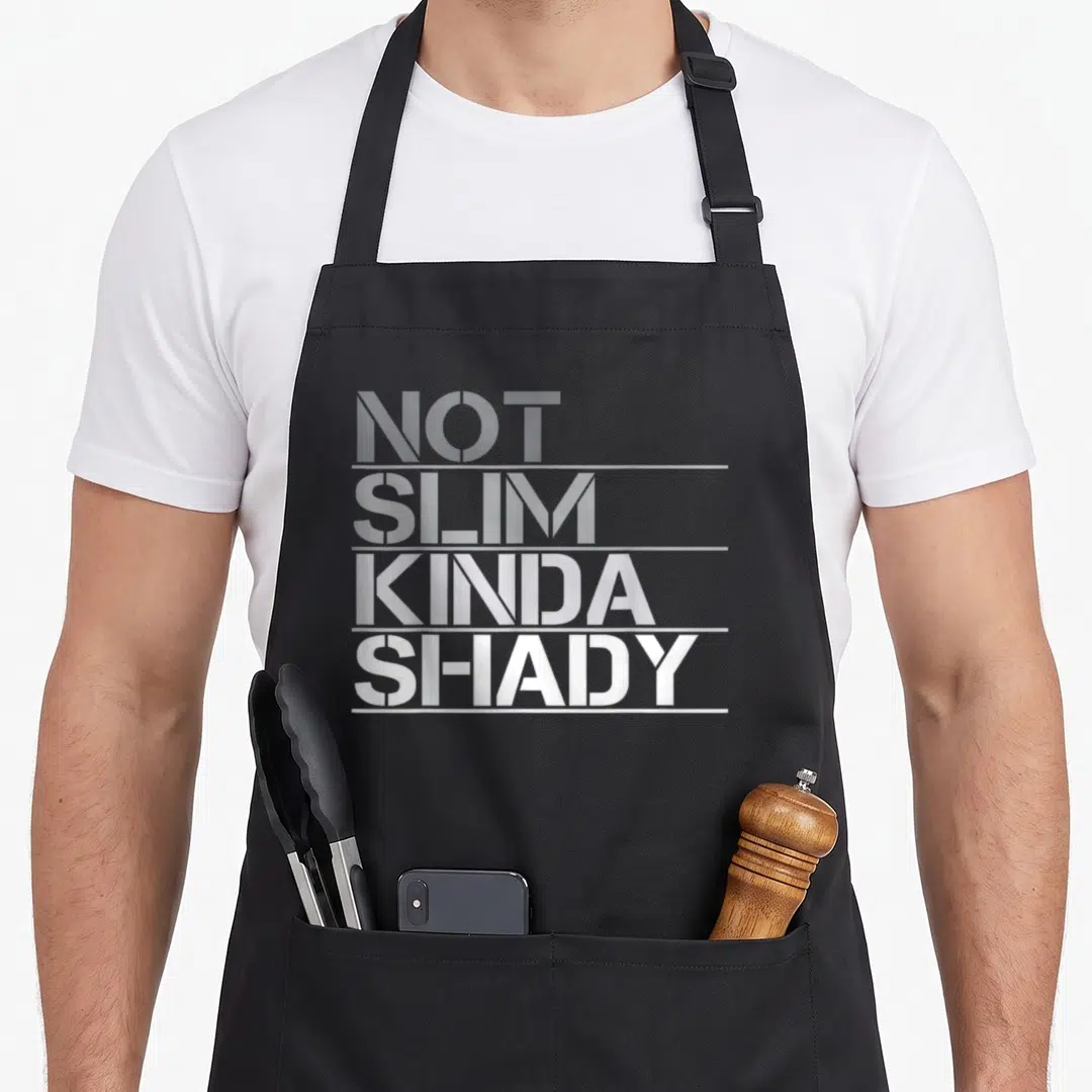 Slim but apron - Stacked white and grey text reading NOT SLIM KINDA SHADY on black background — shown on a black cotton canvas apron against a white background