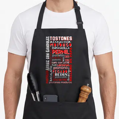 Puerto food aprons - Red and white typography list of Puerto Rican dishes like Mofongo and Lechon on black background — shown on a black cotton canvas apron against a white background