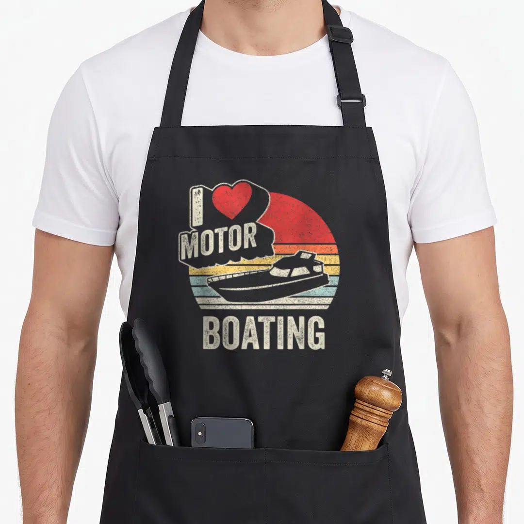 Motor boating apron - Retro boat and striped sun graphic with I MOTOR BOATING text and red heart — shown on a black cotton canvas apron against a white background