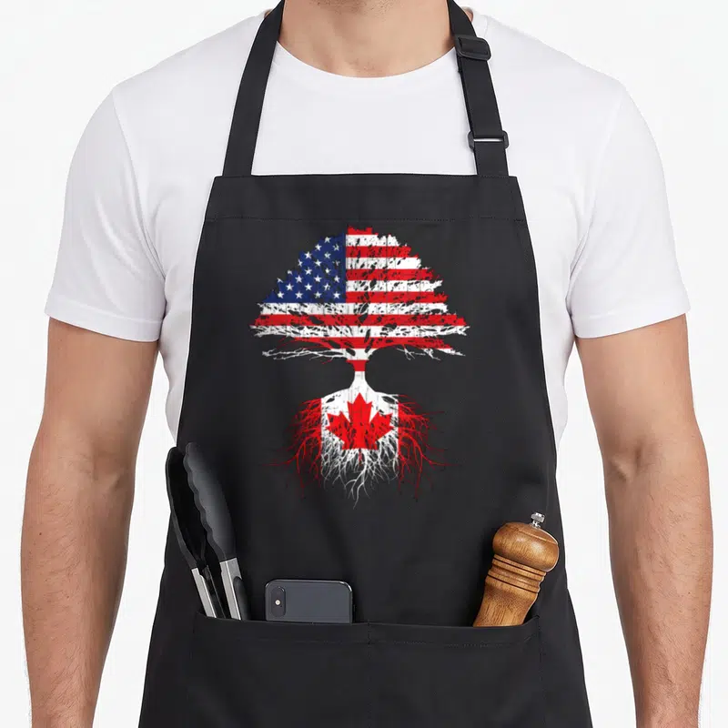 Canadian american flag apron - Tree with USA flag canopy and Canada flag roots in distressed red white blue — shown on a black cotton canvas apron against a white background