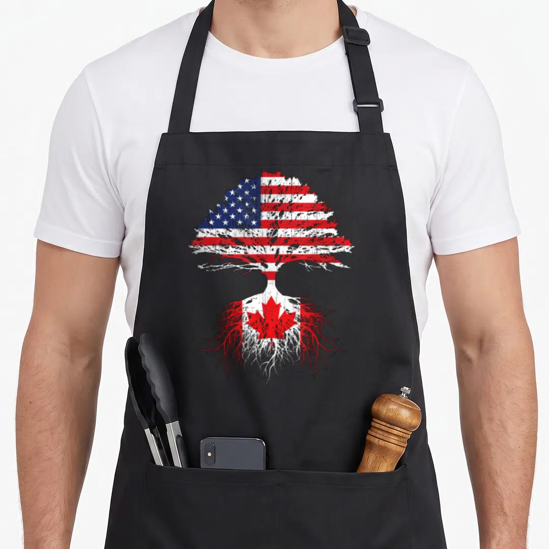 Canadian american flag apron - Tree with USA flag canopy and Canada flag roots in distressed red white blue — shown on a black cotton canvas apron against a white background