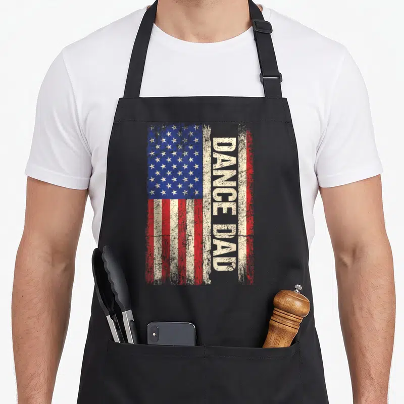 Dance american flag apron - Distressed USA flag with vertical DANCE DAD text and red white blue stripes — shown on a black cotton canvas apron against a white background