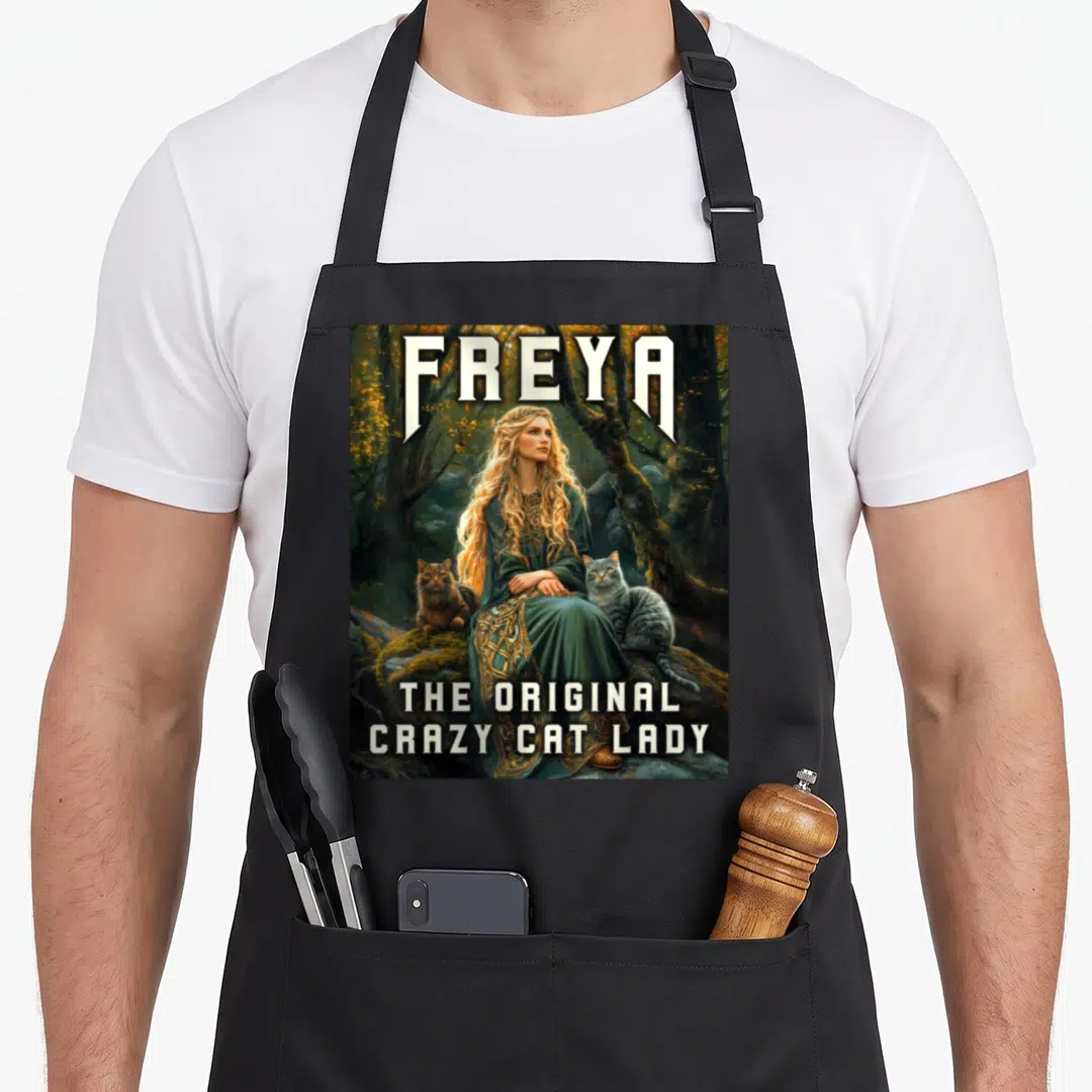 Freya crazy cat lady apron - Woman in green dress with two cats in forest and text FREYA THE ORIGINAL CRAZY CAT LADY — shown on a black cotton canvas apron against a white background