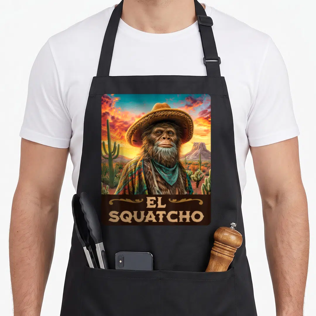 Guardian bigfoot apron - Realistic sasquatch in sombrero and teal bandana with EL SQUATCHO text on desert background — shown on a black cotton canvas apron against a white background