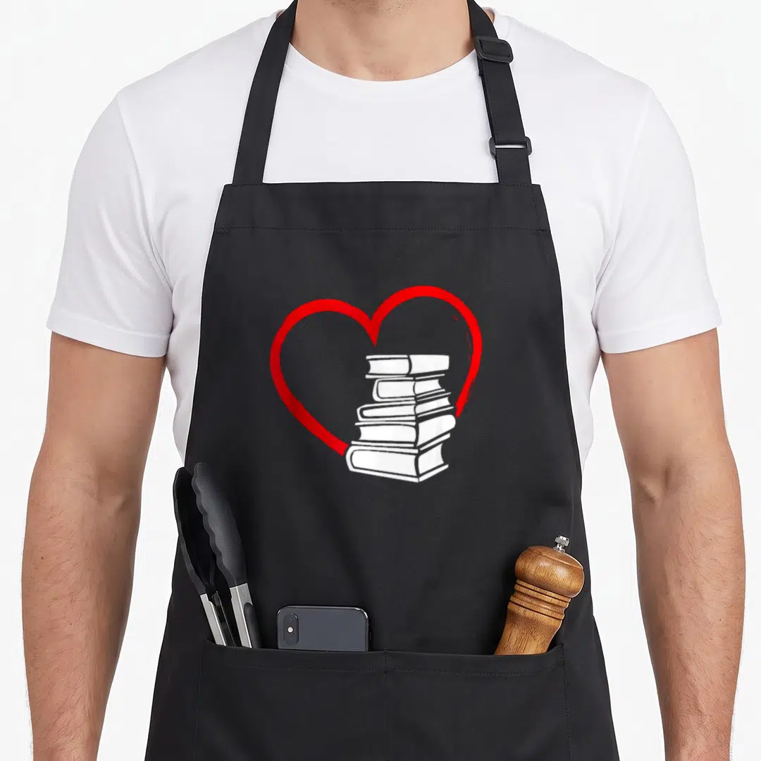 Valentine nerd apron - Red heart outline enclosing a vertical stack of white books in minimalist style — shown on a black cotton canvas apron against a white background