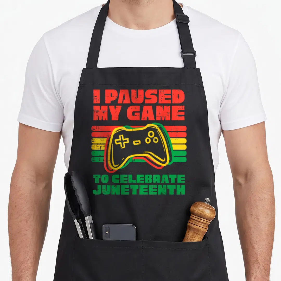 Celebrate game aprons - Distressed game controller over red yellow and green stripes with Juneteenth text — shown on a black cotton canvas apron against a white background