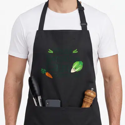 Peas romaine calm and carrot on apron - Stacked text Peas Romaine Calm Carrot with illustrated pea pods lettuce leaf — shown on a black cotton canvas apron against a white background