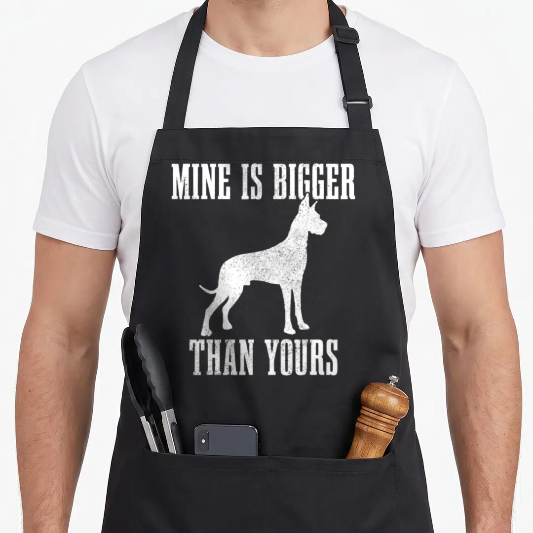 Mine dog apron - White distressed Great Dane silhouette between text MINE IS BIGGER THAN YOURS — shown on a black cotton canvas apron against a white background