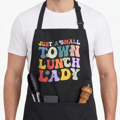 Funny lunch cafeteria aprons - Colorful retro text reading Just A Small Town Lunch Lady surrounded by smiley face — shown on a black cotton canvas apron against a white background