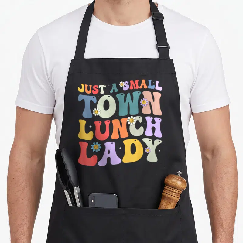 Funny lunch cafeteria aprons - Colorful retro text reading Just A Small Town Lunch Lady surrounded by smiley face — shown on a black cotton canvas apron against a white background