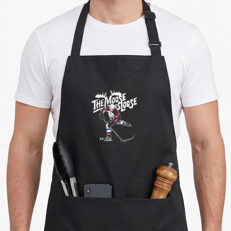 Moose colorado apron - Skating hockey player with THE MOOSE IS LOOSE text in distressed white, maroon, and blue — shown on a black cotton canvas apron against a white background