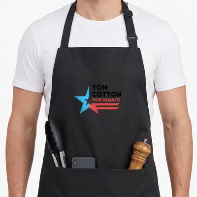 Tom senator apron - TOM COTTON FOR SENATE text beside a split blue red star on black fabric — shown on a black cotton canvas apron against a white background