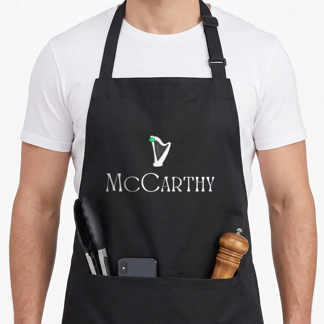 Mccarthy family aprons - White harp with green shamrock above McCARTHY text — shown on a black cotton canvas apron against a white background