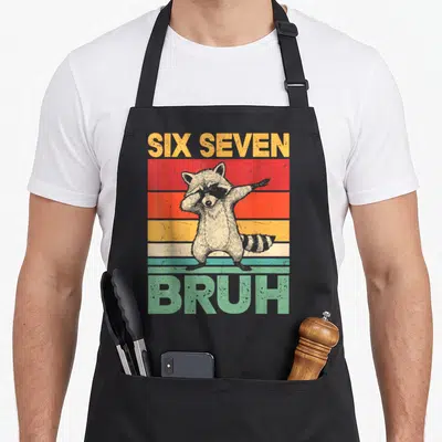 Raccoon meme apron - Dabbing raccoon on retro yellow red orange and mint green stripes with SIX SEVEN BRUH text — shown on a black cotton canvas apron against a white background